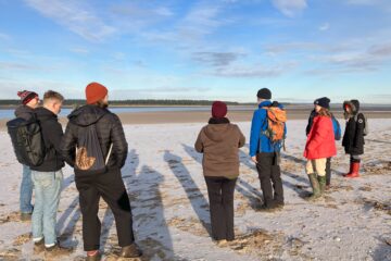 group standing on frosted sand, looking out to the estuary