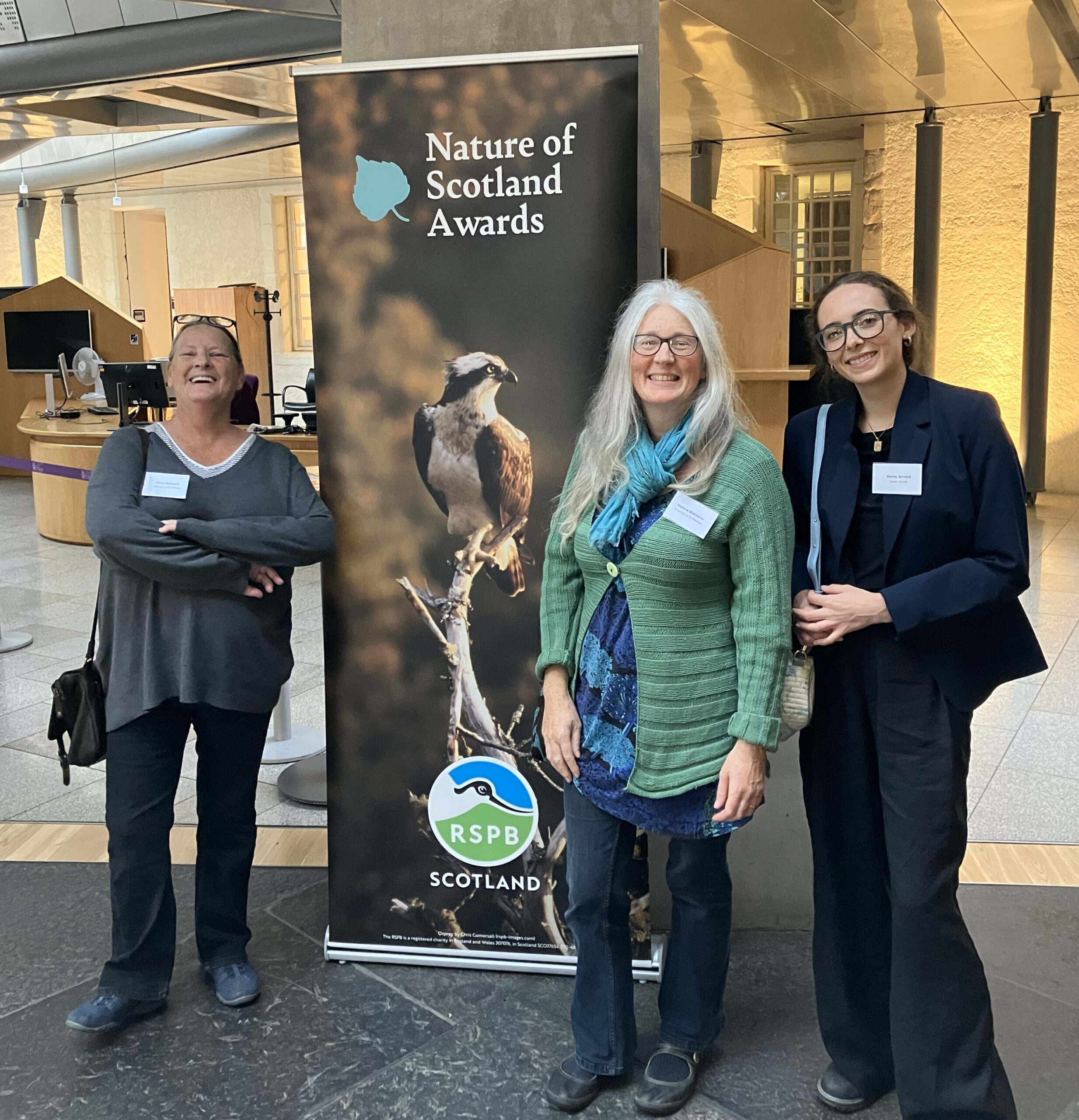 three people smiling beside a Nature of Scotland Awards banner